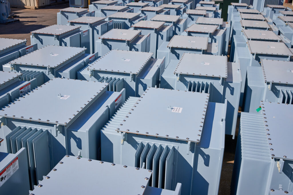 A large number of light blue industrial transformers neatly arranged outdoors, awaiting installation or distribution.